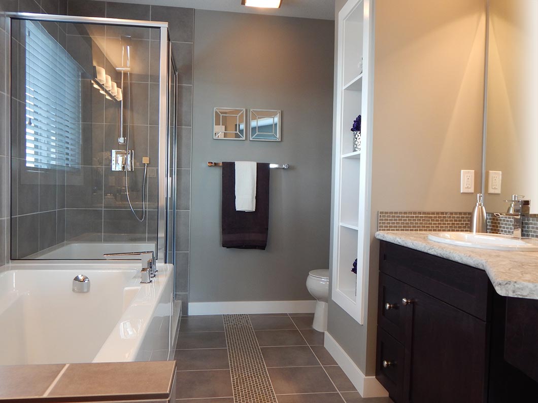 Modern bathrooms feature a large bathtub, glass shower enclosure, wall-mounted towel rack, toilet, open shelves, dark vanity with marble countertop, and tile flooring. Neutral-colored walls and natural light from a window complete the look.