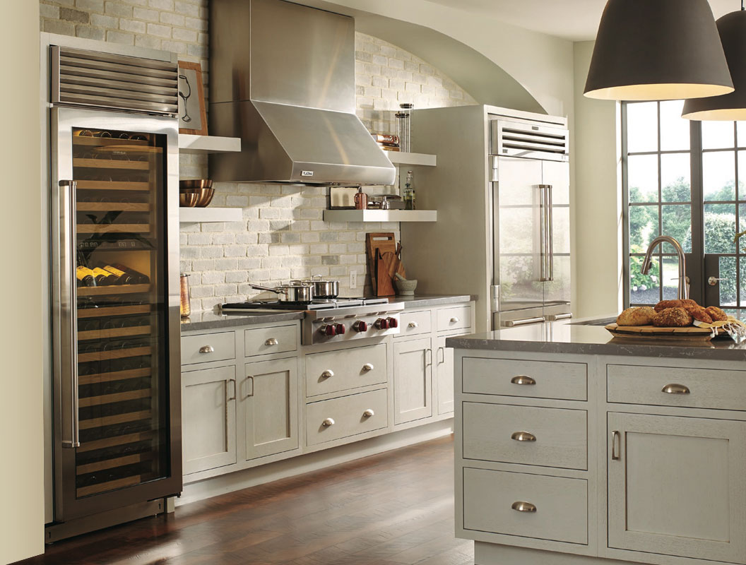 Modern kitchen inspired by classic kitchens, with light cabinets, stainless steel appliances, wine fridge, oven, range hood, kitchen island with bread, large windows for natural light, dark wooden floor, and white brick backsplash.