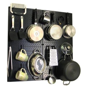 A black pegboard mounted on a wall holds various kitchen utensils, including pots, pans, mugs, graters, and more—all organized and hanging neatly for easy access during spring cooking.