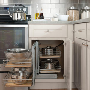 A kitchen with white cabinets and a pull-out corner cabinet organizer holding pots, pans, and bowls. Nearby are a stove, countertop items, and jars of pasta and grains—creating a fresh spring-inspired cooking space.