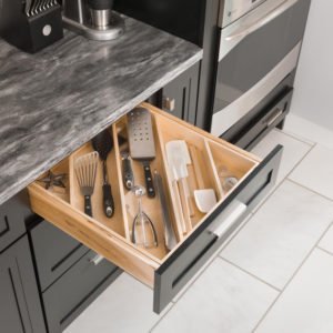 A kitchen drawer with a bamboo organizer holds utensils like spatulas, a whisk, and measuring spoons, perfectly organized for spring cooking under a gray countertop with black cabinets.